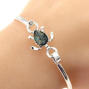 Può includere: Braccialetto rigido in argento con un ciondolo a scorpione in argento con una conchiglia di abalone iridescente.