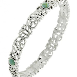 May include: Silver bangle bracelet with an openwork filigree design. The bracelet has two oval turquoise-coloured stones. The intricate metalwork creates a delicate and ornate appearance, suitable for adding a touch of elegance to any outfit.