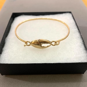 May include: A gold-toned bangle bracelet featuring a central crab claw charm. The thin, circular metal band connects to the claw ornament on both sides with small, integrated loops, creating a continuous, lightweight piece of jewelry.