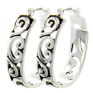 Op de afbeelding: Een paar zilveren oorringen met een open ontwerp. De oorbellen hebben een gedetailleerd patroon van wervelende lijnen en rondingen, wat een sierlijke en elegante uitstraling cre&euml;ert. De oorringen zijn van een gemiddelde grootte.