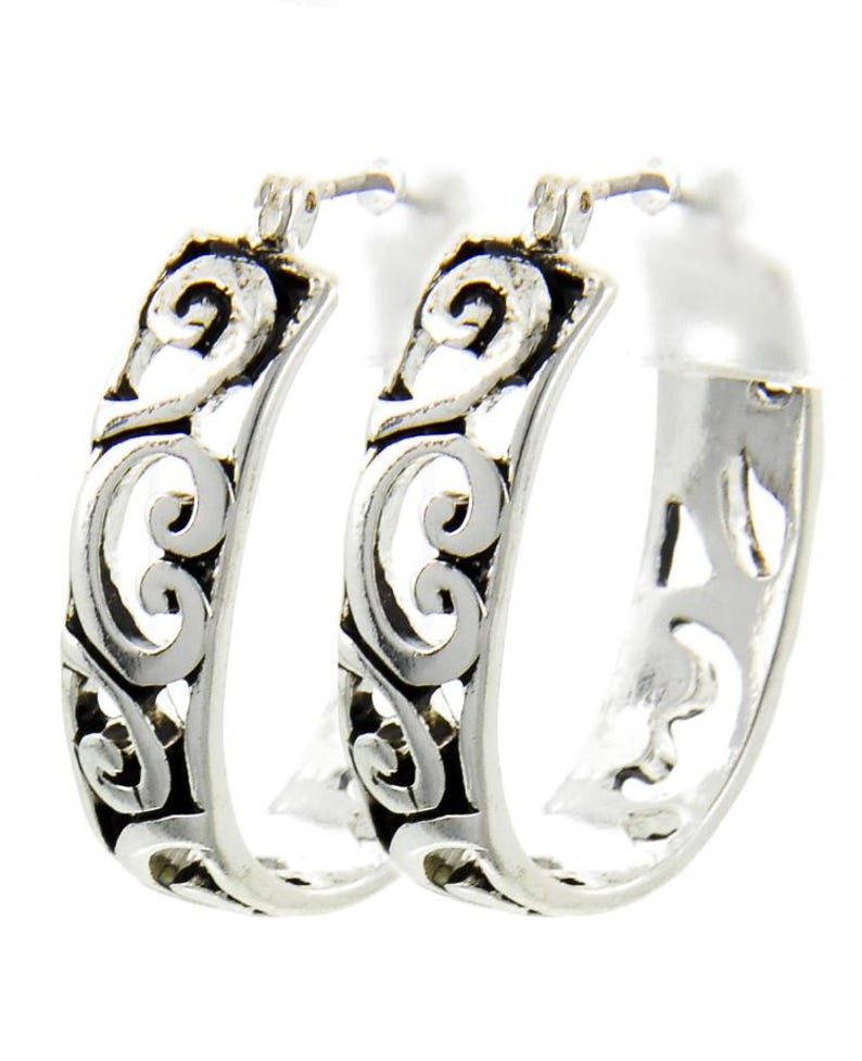 Op de afbeelding: Een paar zilveren oorringen met een open ontwerp. De oorbellen hebben een gedetailleerd patroon van wervelende lijnen en rondingen, wat een sierlijke en elegante uitstraling cre&euml;ert. De oorringen zijn van een gemiddelde grootte.