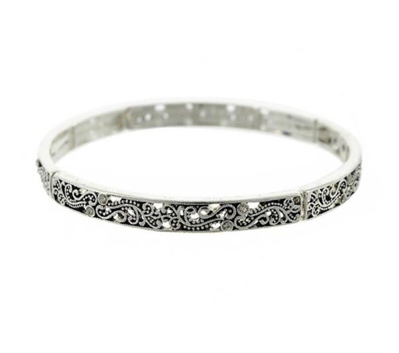 May include: A silver bangle bracelet with an intricate floral design. The bracelet is made of metal and has a delicate, feminine look.