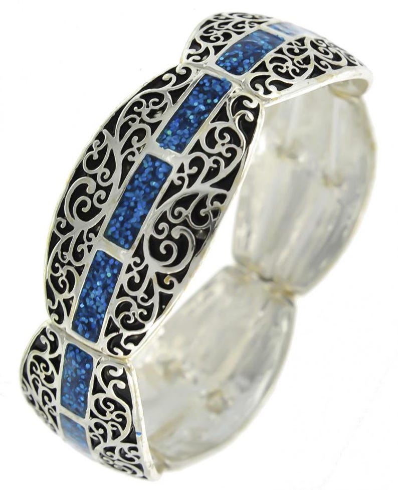 Pu&ograve; includere: Bracciale argentato con filigrana nera e inserti rettangolari blu glitterati. Il bracciale ha un design ornato con una fascia elastica. Un accessorio di moda.
