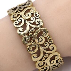 Może przedstawiać: Bransoletka z metalu w kolorze złotym z ozdobnym, skomplikowanym, ażurowym wzorem z wirujących, kwiatowych wzor&oacute;w.