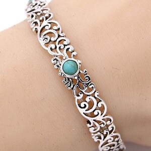 May include: Silver filigree bracelet with turquoise stone details. The bracelet has an openwork design with scrolling patterns and turquoise stones. A decorative piece of jewellery.