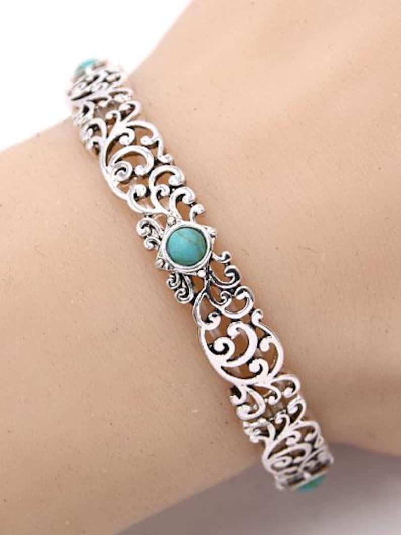 May include: Silver filigree bracelet with turquoise stone details. The bracelet has an openwork design with scrolling patterns and turquoise stones. A decorative piece of jewellery.