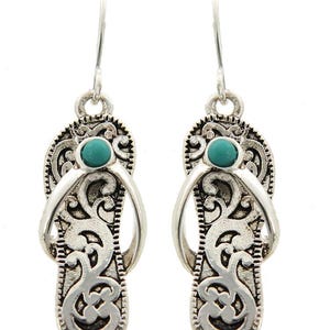 May include: Silver dangle earrings with a turquoise stone in the center of each earring. The earrings are shaped like flip flops with an intricate design.