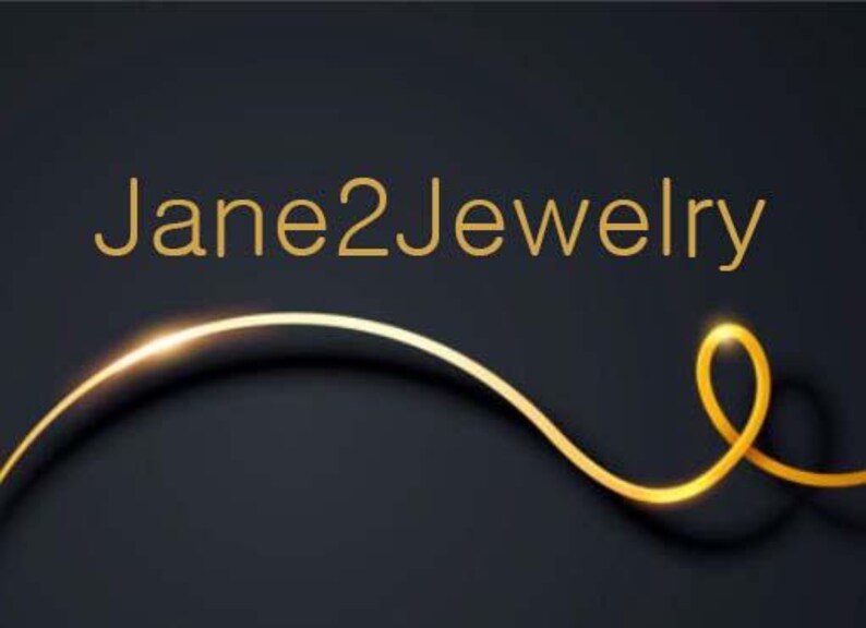 May include: A gold-colored logo with the text "Jane2Jewelry" on a black background. A gold-colored line curves across the bottom of the image.