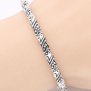 May include: A silver bangle bracelet with an intricate, ornate design. The bracelet is made of metal and has a smooth, polished finish.