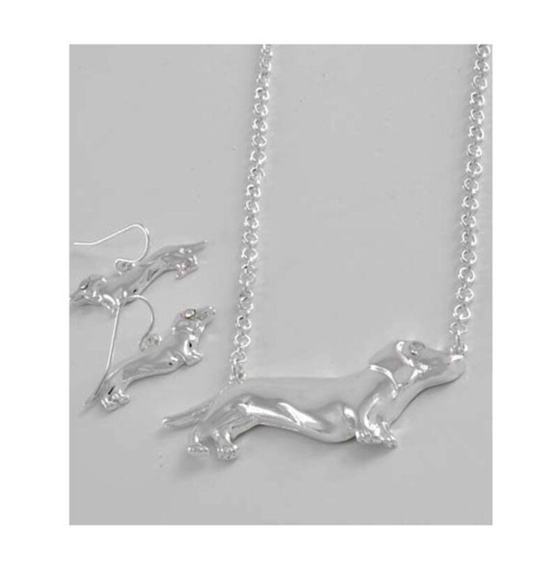 May include: Silver dachshund necklace and earrings set. The necklace features a dachshund pendant with a silver chain. The earrings are silver dachshund studs.
