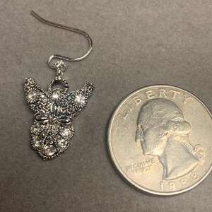 May include: Silver angel dangle earrings with clear crystal accents. The earrings are about the size of a quarter.