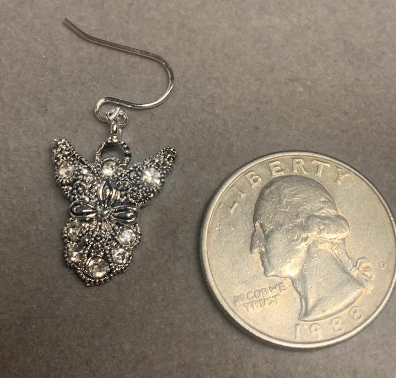 May include: Silver angel dangle earrings with clear crystal accents. The earrings are about the size of a quarter.