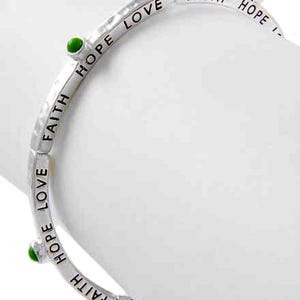 May include: Silver-toned bracelet with the words "FAITH," "HOPE," and "LOVE" engraved. The bracelet has three small green beads and is curved. The bracelet is on a white background.