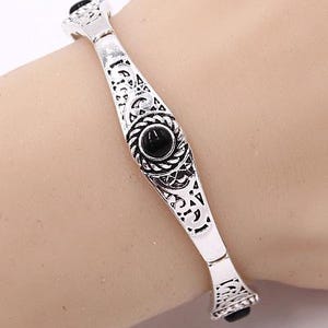 May include: Silver bracelet with an intricate design and black gemstones.