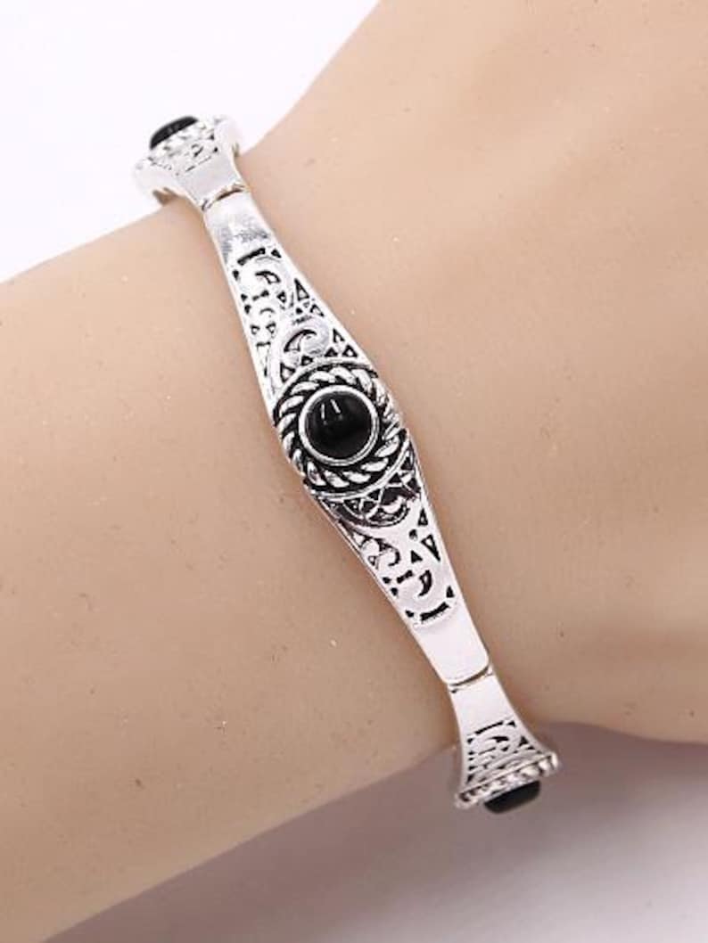 May include: Silver bracelet with an intricate design and black gemstones.
