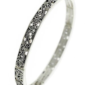 May include: A silver bangle bracelet with a delicate, intricate floral design. The design is black and features small, clear rhinestones.
