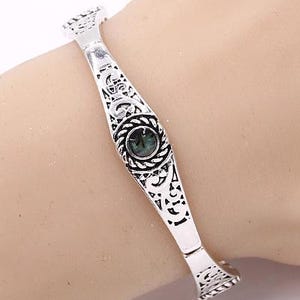 May include: Silver bangle bracelet with an ornate design and a green gemstone in the centre.