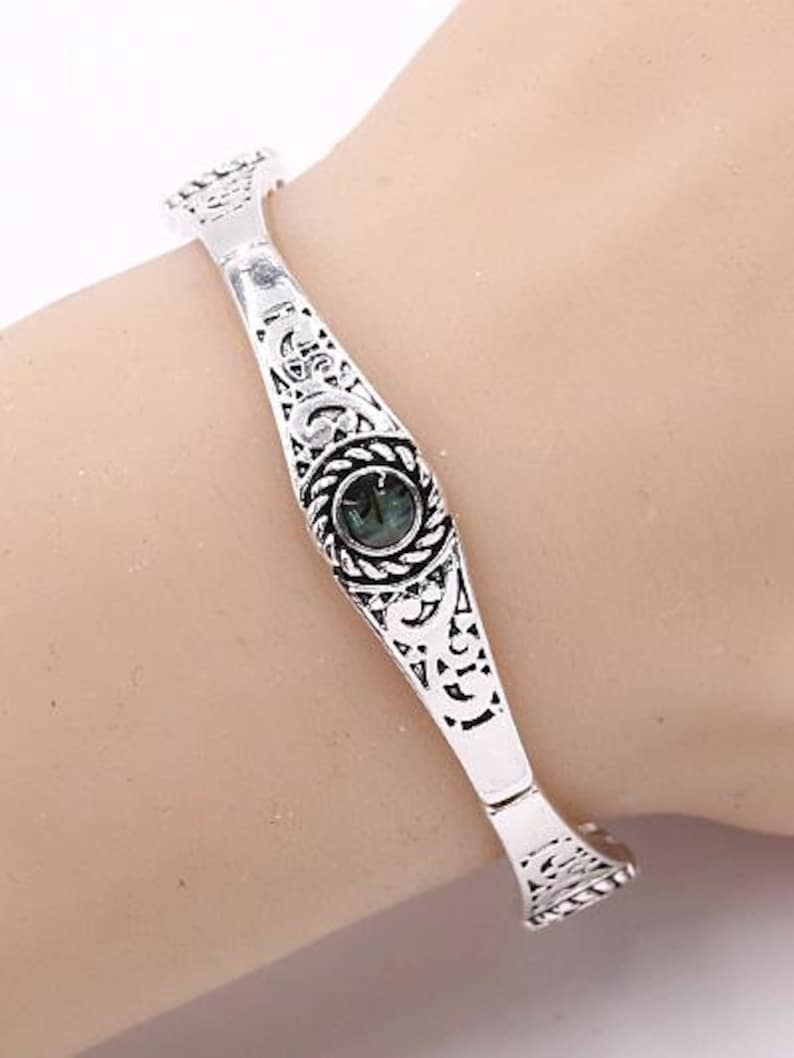 May include: Silver bangle bracelet with an ornate design and a green gemstone in the centre.