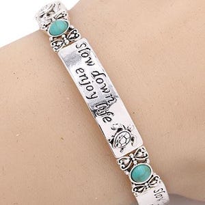 Peut inclure: Bracelet argent&eacute; orn&eacute; de pierres ovales turquoise et de l'inscription grav&eacute;e &laquo;&nbsp;Slow down enjoy life&nbsp;&raquo;. Le bracelet pr&eacute;sente des motifs d&eacute;coratifs de papillons et de tortues.