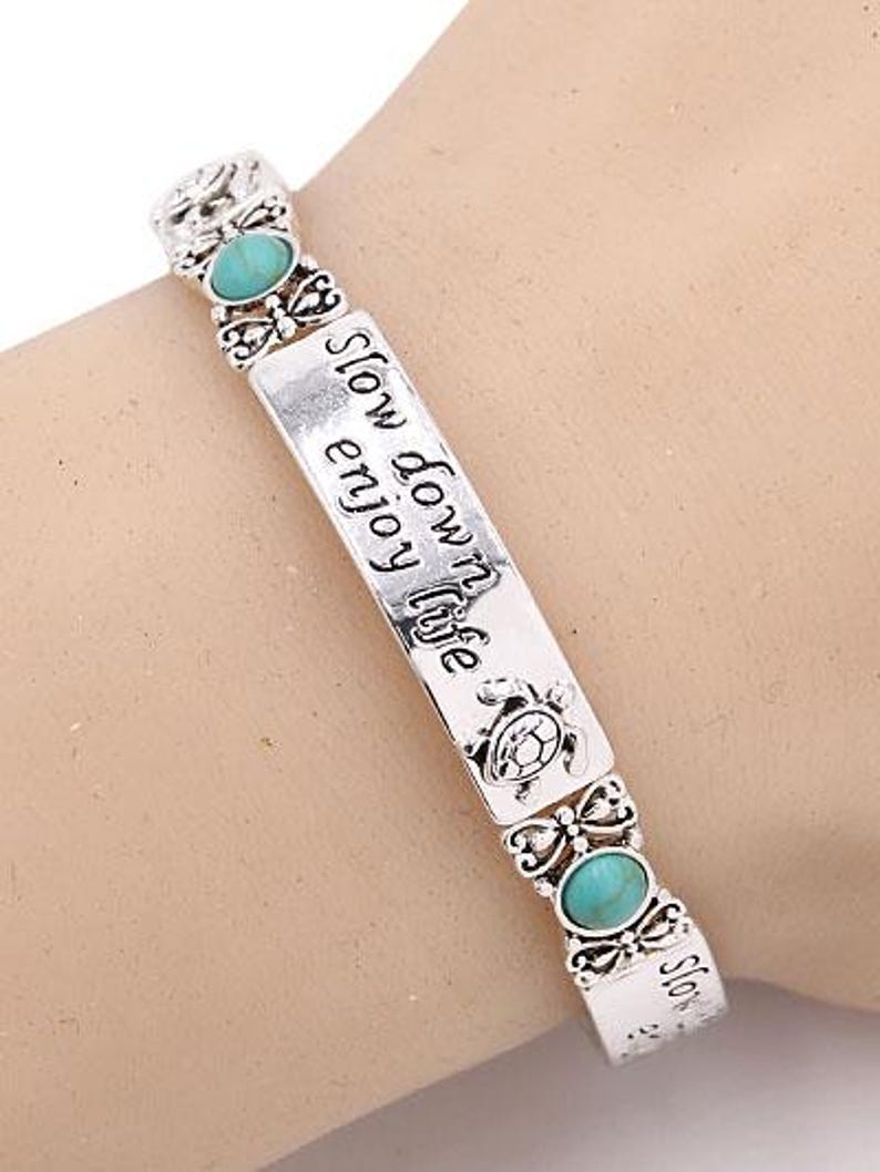 Peut inclure: Bracelet argent&eacute; orn&eacute; de pierres ovales turquoise et de l'inscription grav&eacute;e &laquo;&nbsp;Slow down enjoy life&nbsp;&raquo;. Le bracelet pr&eacute;sente des motifs d&eacute;coratifs de papillons et de tortues.