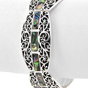 Pu&ograve; includere: Un braccialetto argentato con un design a filigrana e intarsi rettangolari in conchiglia di abalone. Il braccialetto presenta intricati motivi traforati e colori iridescenti all'interno dell'abalone. Il braccialetto &egrave; mostrato su sfondo bianco.