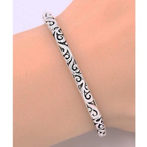 Puede incluir: Un brazalete de plata con un dise&ntilde;o intrincado y en espiral.