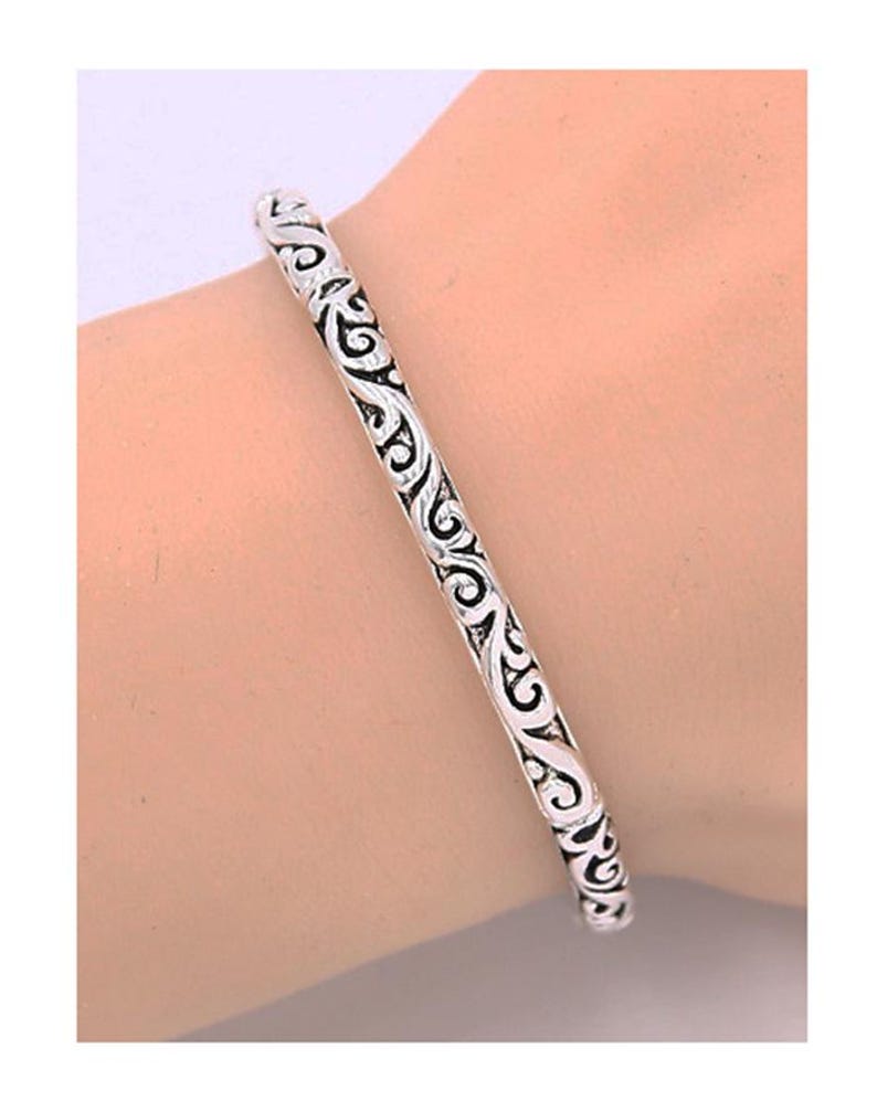 Puede incluir: Un brazalete de plata con un dise&ntilde;o intrincado y en espiral.