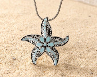 May include: A silver-toned metal starfish pendant necklace featuring intricate textured detailing and light blue enamel accents on each of the five arms. The pendant hangs from a thin, flexible silver-toned snake chain necklace.