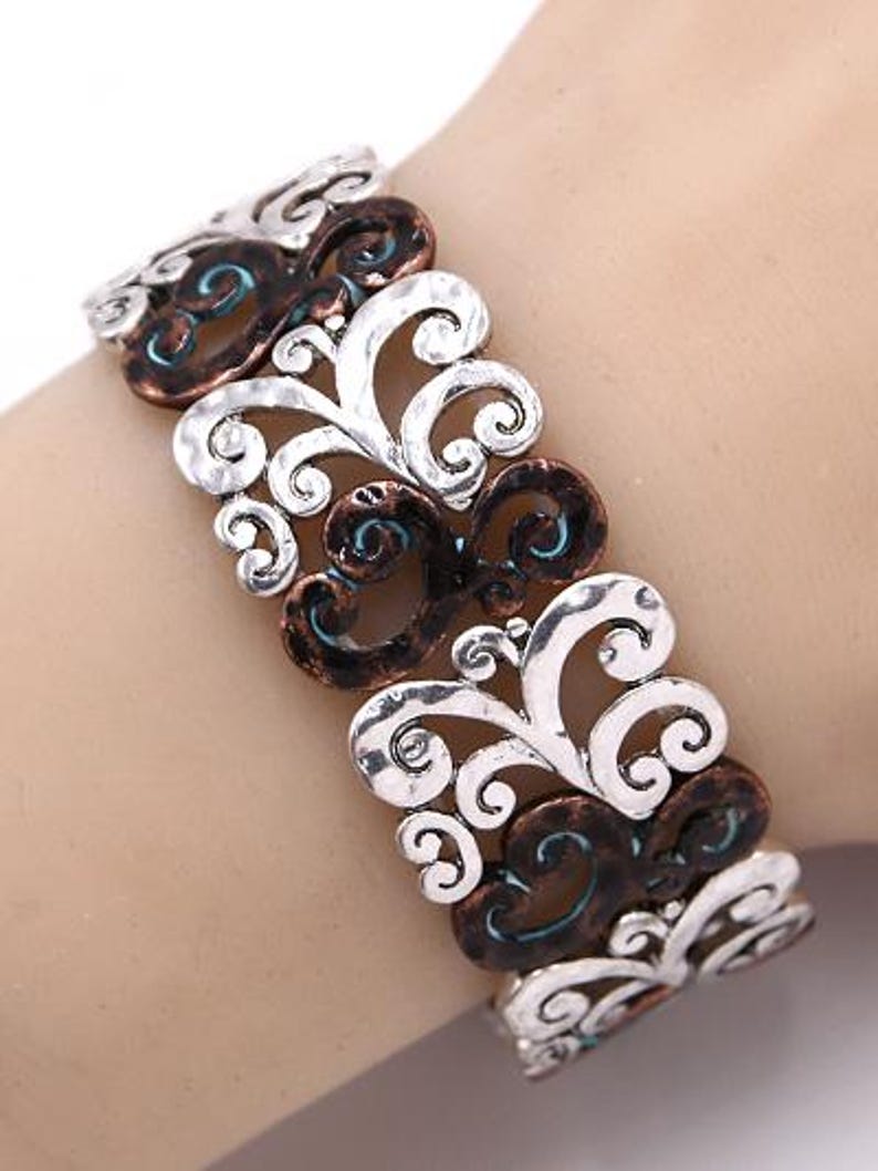 Może przedstawiać: Bransoletka srebrna i miedziana z kręconym wzorem kwiatowym. Bransoletka jest wykonana z metalu i ma fakturowane wykończenie.