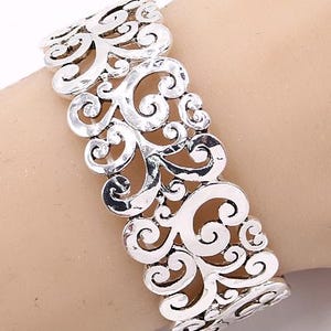 Może przedstawiać: Srebrna bransoletka z filigranu o delikatnym, skomplikowanym wzorze. Bransoletka jest otwarta i regulowana, aby pasowała do większości nadgarstk&oacute;w.