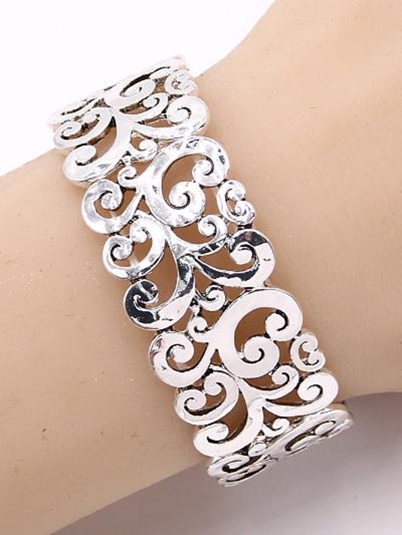 Może przedstawiać: Srebrna bransoletka z filigranu o delikatnym, skomplikowanym wzorze. Bransoletka jest otwarta i regulowana, aby pasowała do większości nadgarstk&oacute;w.