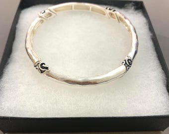 Peut inclure: Un bracelet jonc de couleur argentée avec une surface lisse et arrondie, ponctué de segments décoratifs texturés aux accents sombres. Le bracelet présente un design circulaire continu avec une finition métallique polie et des détails complexes.