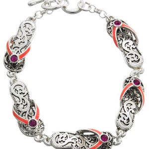 May include: Silver bracelet with five flip-flop charms. Each charm is detailed with an intricate design and features a pink rhinestone. The flip-flops are painted a bright orange color.