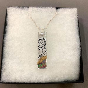 May include: A rectangular silver pendant necklace featuring a black etched tree design on the upper portion, a curved gold-toned accent, and a rectangular iridescent opal inlay at the base, suspended from a delicate silver chain.