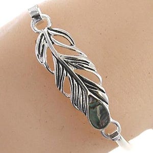 May include: Silver bracelet with a feather charm featuring a green abalone shell inlay.