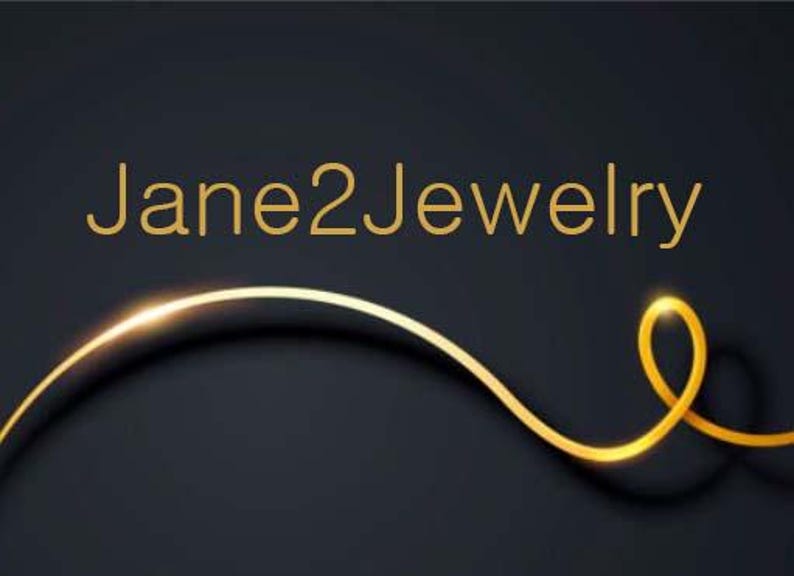 Peut inclure: Un logo de couleur or avec le texte "Jane2Jewelry" sur un fond noir. Une ligne de couleur or courbe en bas de l'image.