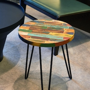 May include: A small round side table with a colorful, multi-colored wood top and black metal legs. The table top is made of reclaimed wood with a distressed finish.