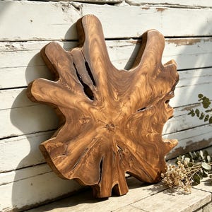 May include: A natural wood slab with a live edge, featuring a prominent star-shaped silhouette and intricate, swirling grain patterns in shades of golden brown and tan. The surface displays deep, dark fissures and a smooth, polished finish.