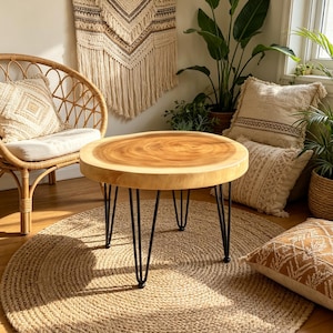 May include: A round coffee table featuring a natural light-colored wood slab top with visible grain patterns and smooth edges, supported by four thin black metal hairpin legs. The table surface displays a circular wood grain design.