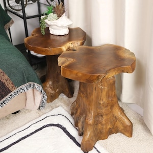 May include: Two wooden end tables made from natural tree trunks. The tables have a round top and a thick, irregular base. The tables are made of a light brown wood with a natural finish.