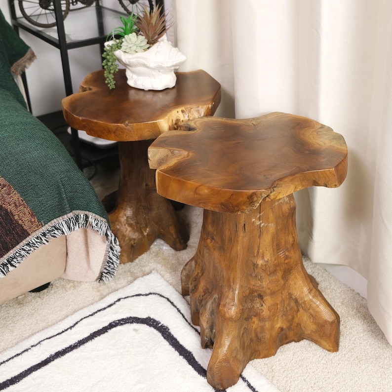 May include: Two wooden end tables made from natural tree trunks. The tables have a round top and a thick, irregular base. The tables are made of a light brown wood with a natural finish.