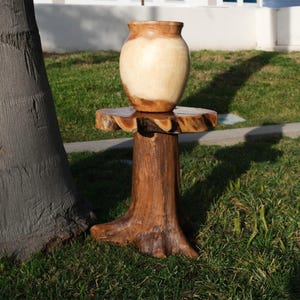 May include: A wooden table with a tree trunk base and a round top. A light brown wooden vase sits on the table.