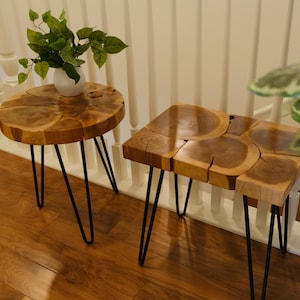May include: Two wooden side tables with black hairpin legs. One table is round, the other is square. The tables have a natural wood grain finish. A white vase with green leaves sits on the round table.