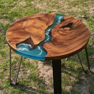 May include: Round wooden table with a blue and white epoxy resin river design. The table has black metal legs.
