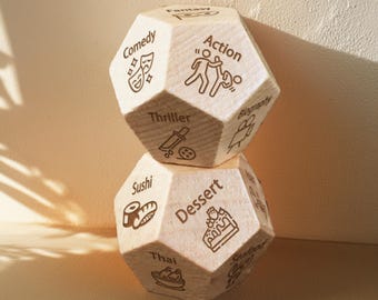 May include: A wooden dice with different categories on each side. The categories include: Comedy, Action, Thriller, Fantasy, Biography, Sushi, Dessert, Thai, and History. The dice is stacked on top of another dice.