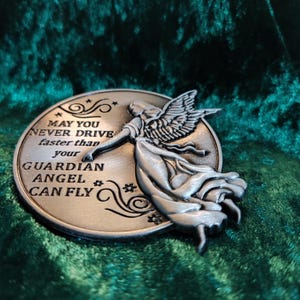 Könnte beinhalten: Ein silberfarbener Metallanhänger mit einem Schutzengel-Motiv und der Inschrift "Möge du nie schneller fahren als dein Schutzengel fliegen kann".