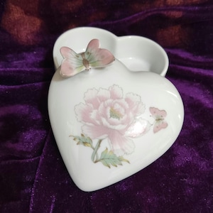 Puede incluir: Caja de porcelana blanca en forma de corazón con un diseño de flor rosa y mariposa. La tapa presenta una mariposa 3D.