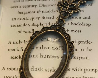 May include: Antique brass-toned oval pendant necklace with a clear glass center. The pendant has an ornate filigree design and hangs from a matching chain. The background features text from a perfume advertisement.