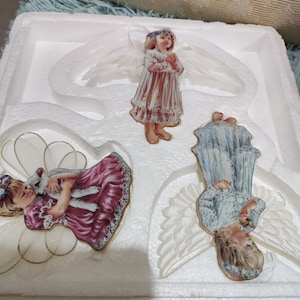 Peut inclure: Trois ornements d'anges en porcelaine avec des ailes. Un ange tient un agneau, un autre prie et le troisième tient une fleur. Les anges portent tous des robes blanches avec des garnitures dorées.