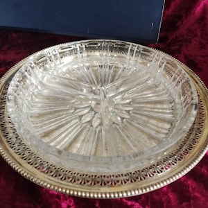 Peut inclure: Un plateau de service argenté avec un plat en verre transparent à trois sections. Le plat en verre présente un motif en forme d'éclat d'étoile au centre. Le plateau a un bord décoratif ajouré et est posé sur un fond rouge foncé.